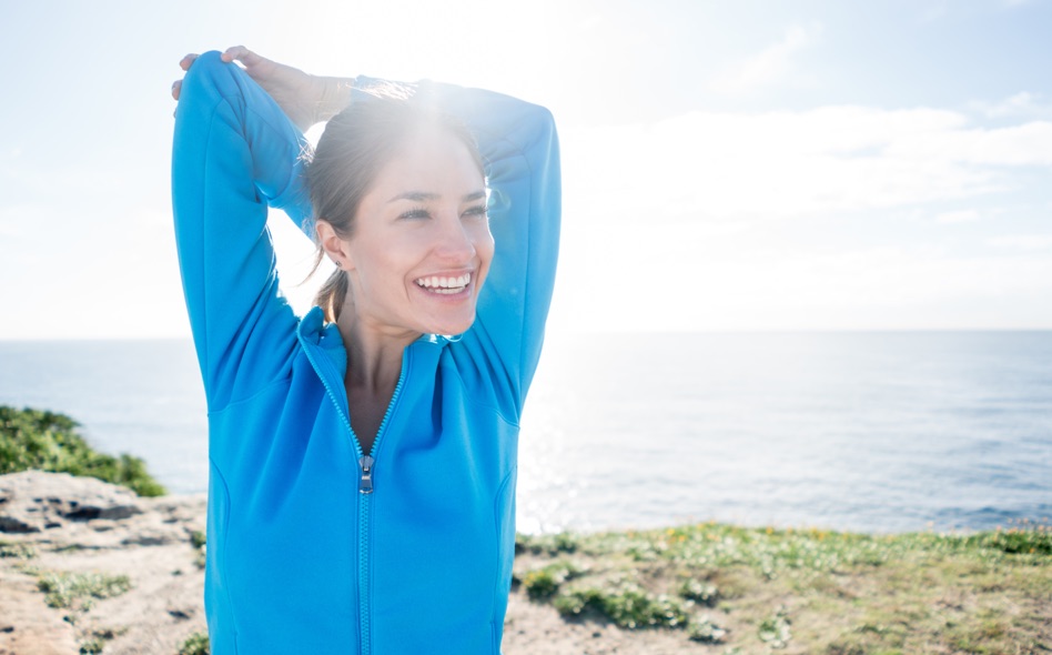Athletic woman in a blue jacket stretching her arms before a workout