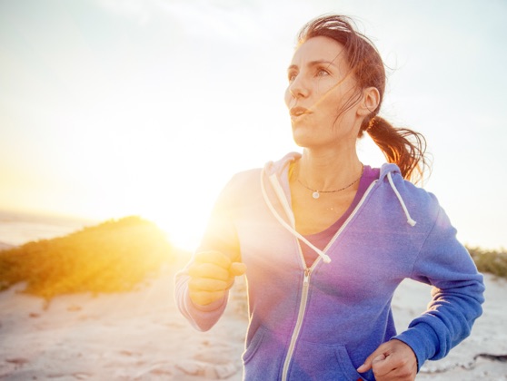 Woman in a purple hoodie running on the beach at sunset