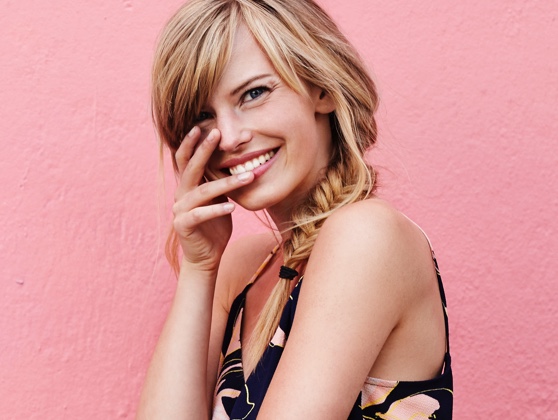 Young woman with clear skin smiling in front of a pink background