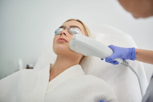 A woman receiving a professional laser facial treatment while wearing protective goggles, showcasing the benefits of a laser facial for smoother and rejuvenated skin.